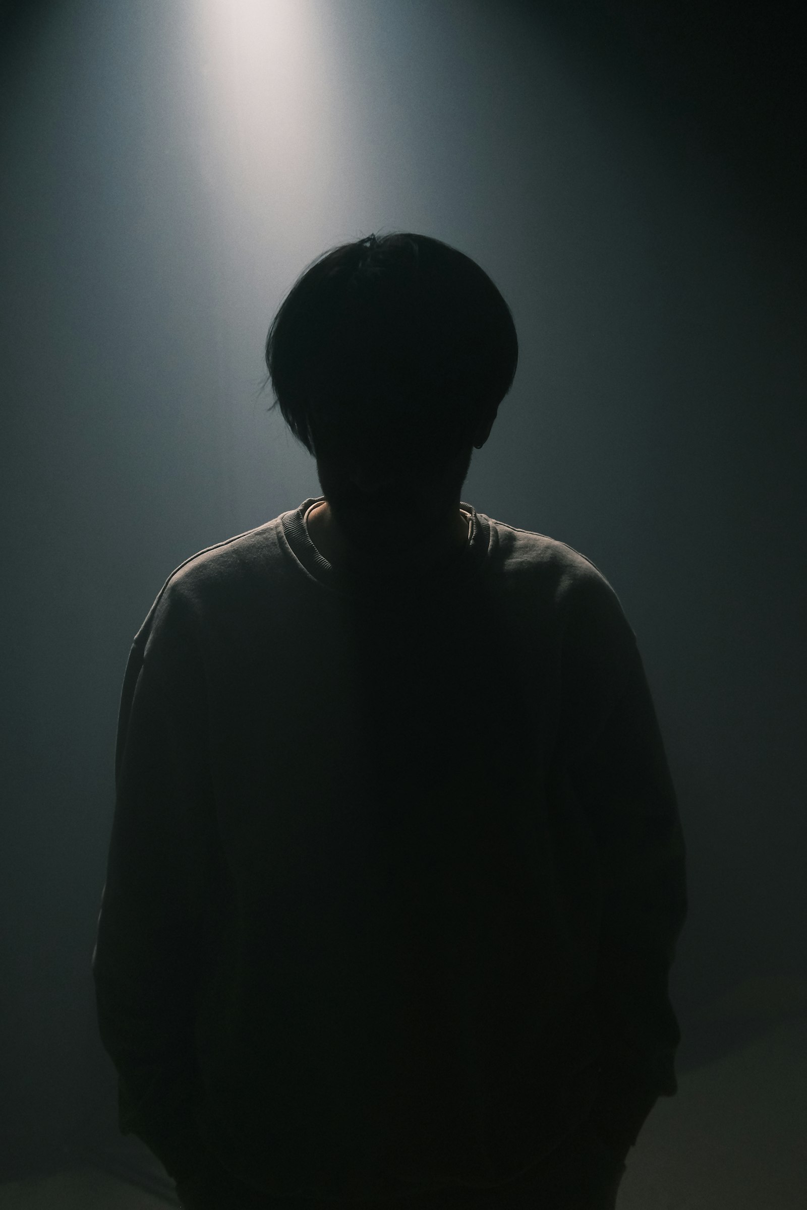Lone figure lit by a single hard beam in a dark room, the cold dread tone horror titles trade on
